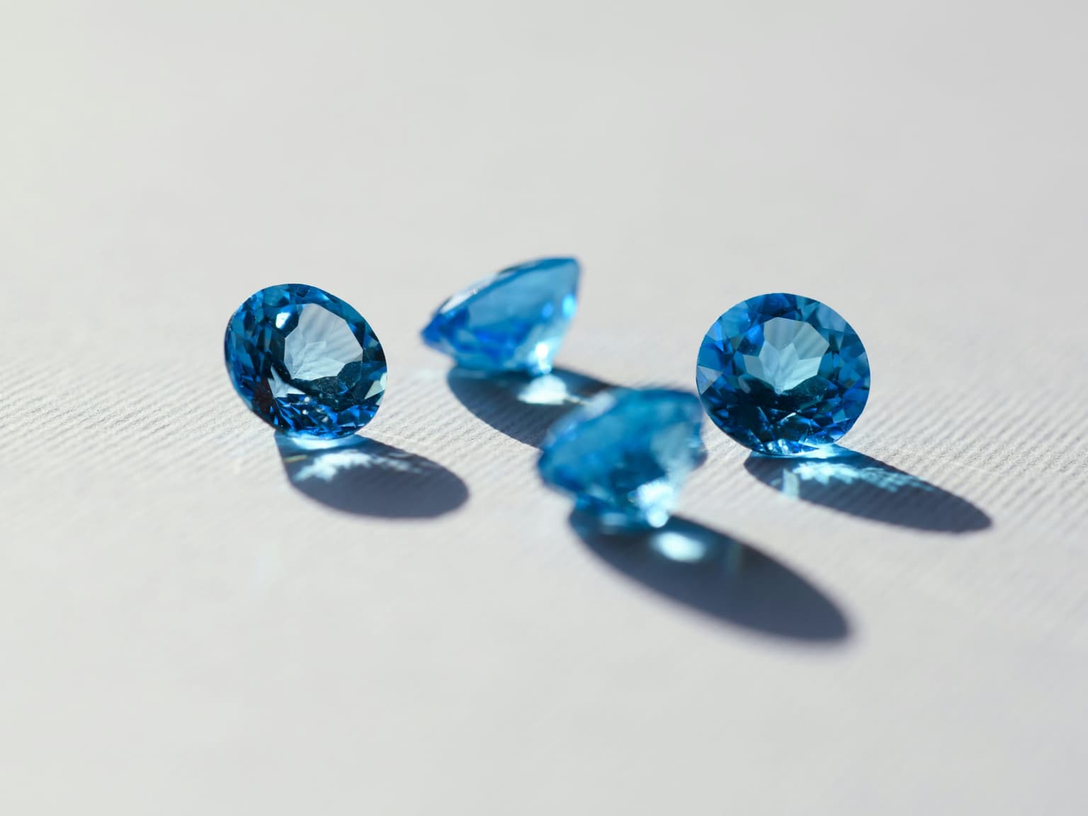 Four round brilliant-cut blue stones arranged on a white surface, each casting a long shadow
