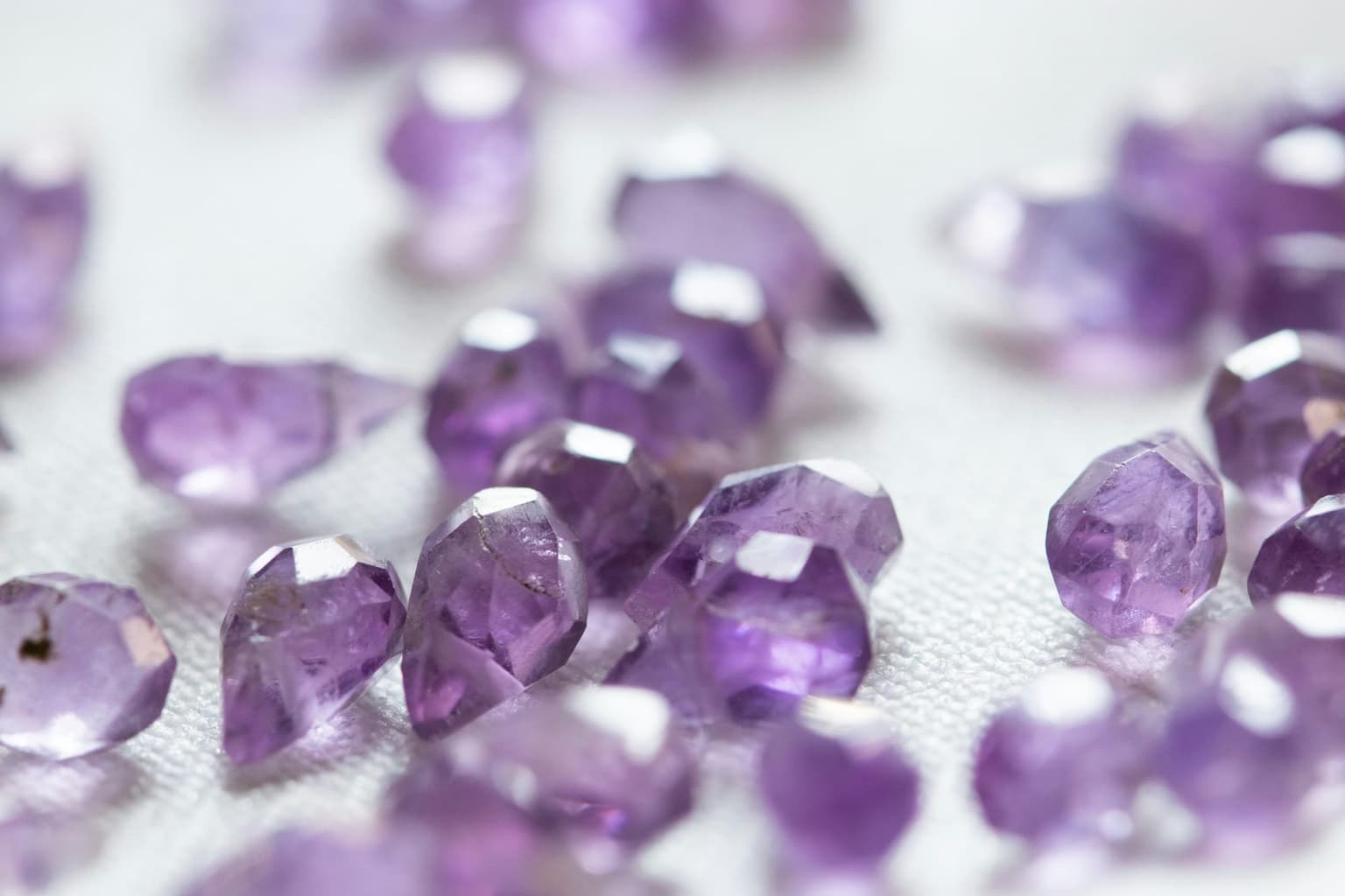 Many small lilac faceted stones scattered on a pale surface, photographed with shallow depth of field