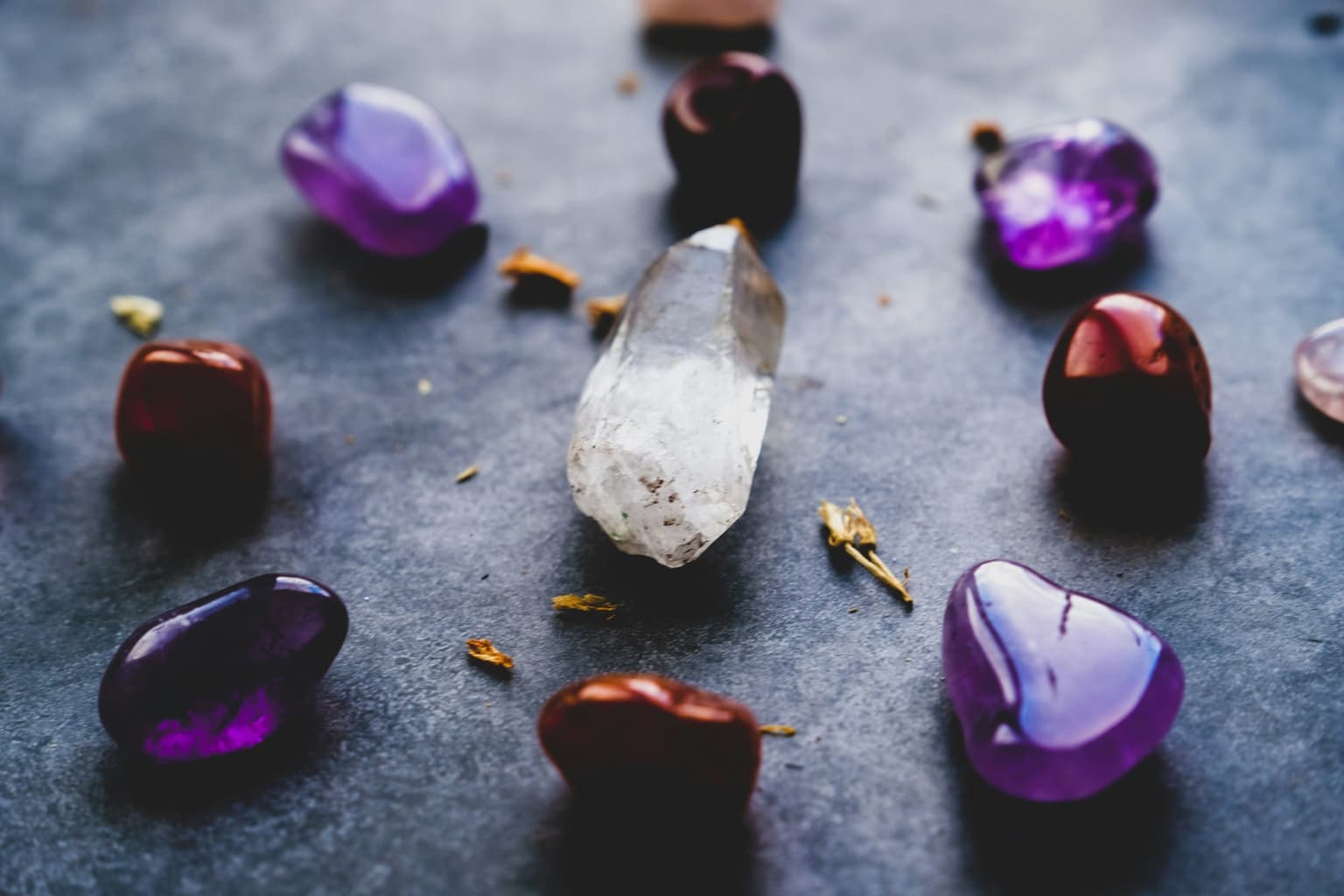An assortment of polished and rough stones in purple, red and clear, scattered across a grey slate surface