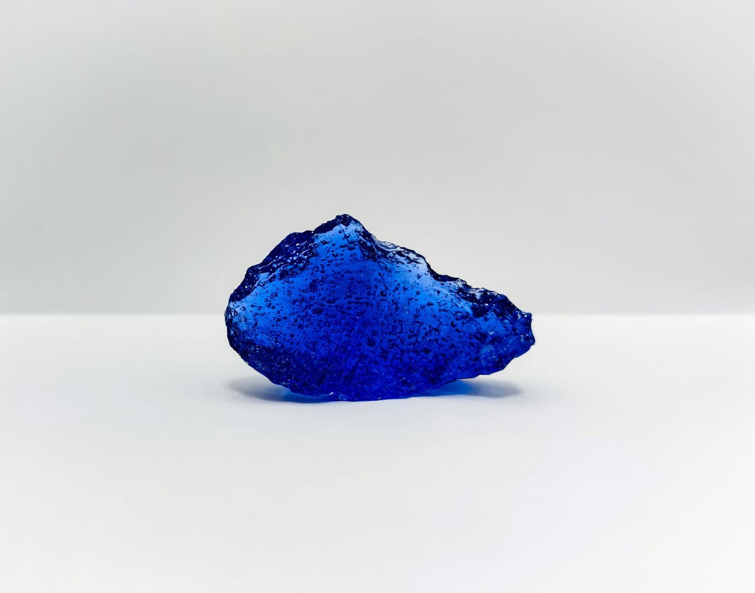 A single piece of rough, uncut blue mineral resting on a white surface