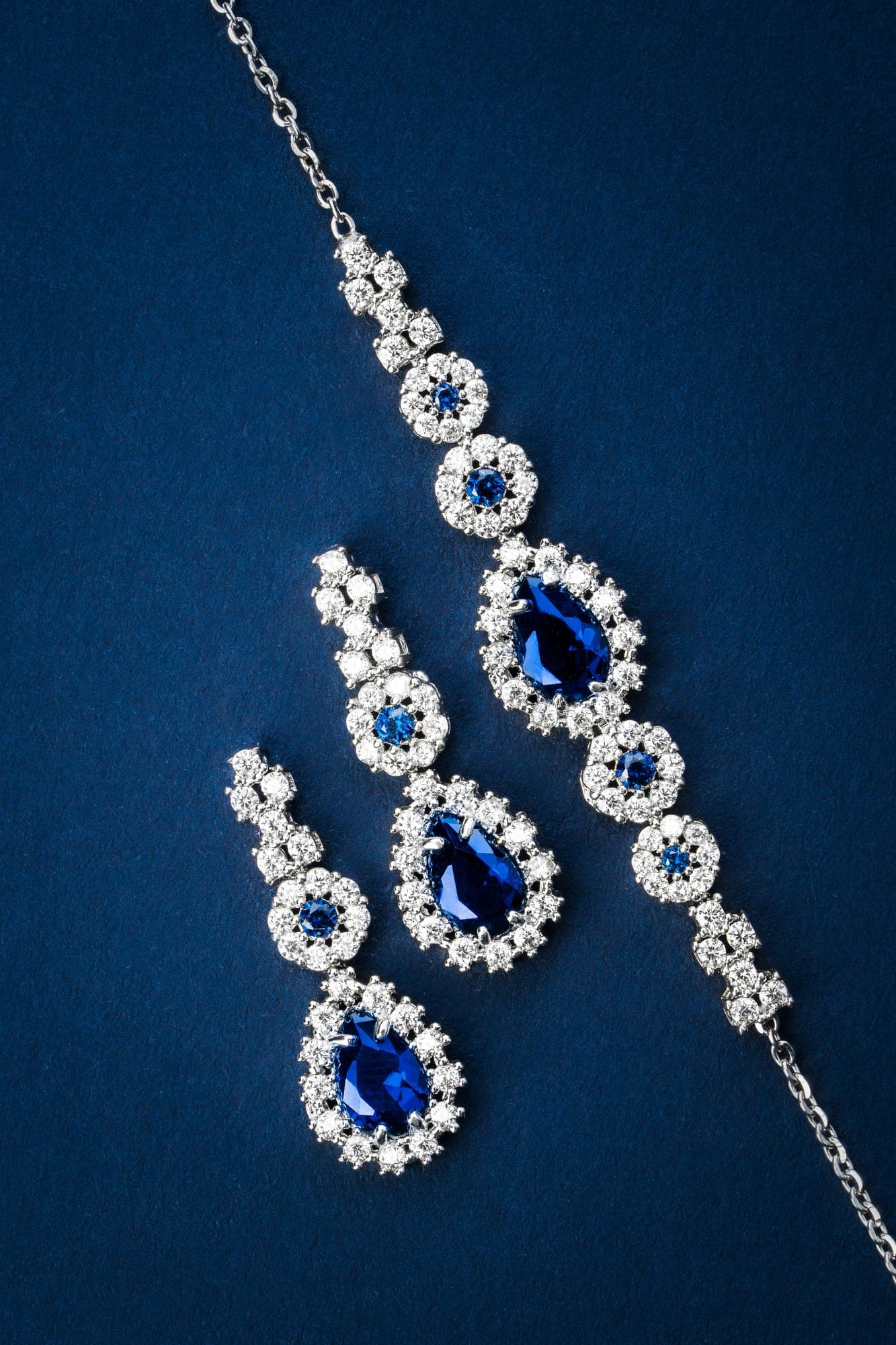 A bracelet and drop earrings set with blue stones and small colourless stones, arranged on deep blue fabric